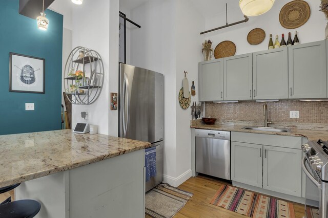 kitchen featuring decorative backsplash, a breakfast bar, light stone countertops, stainless steel appliances, and a sink