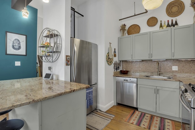 kitchen featuring stainless steel appliances, a sink, light wood-style flooring, tasteful backsplash, and light stone counters