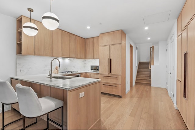 kitchen featuring a peninsula, light brown cabinetry, light wood-style floors, a kitchen bar, and a sink