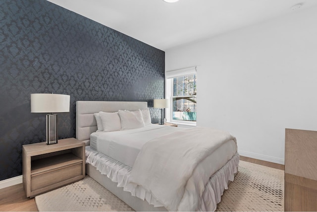 bedroom featuring baseboards, an accent wall, wood finished floors, and wallpapered walls