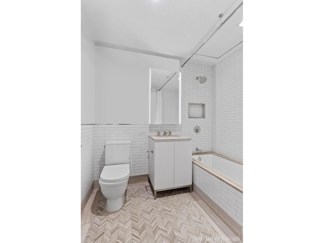 full bath featuring tiled shower / bath combo, tile patterned flooring, tile walls, toilet, and vanity