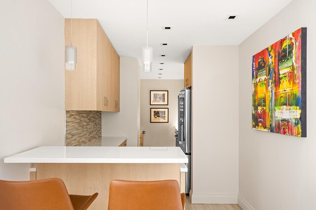 kitchen featuring a breakfast bar, light countertops, decorative backsplash, freestanding refrigerator, and a peninsula