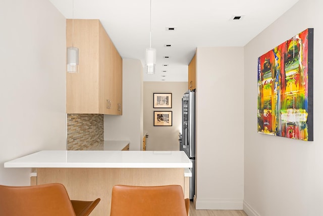 kitchen with tasteful backsplash, freestanding refrigerator, a peninsula, light wood finished floors, and light countertops