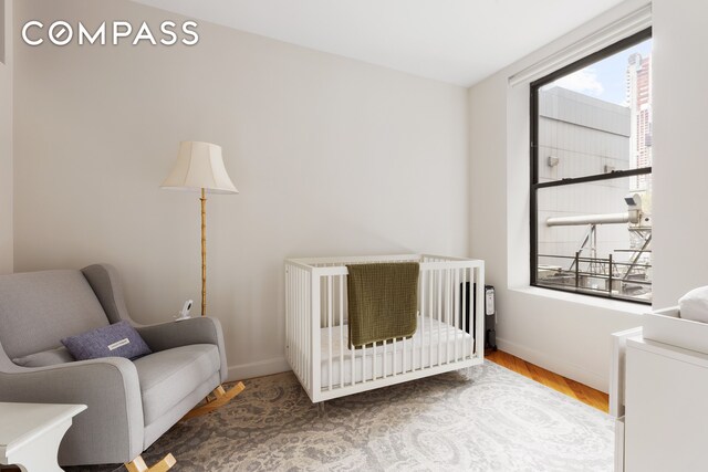 bedroom with a nursery area, baseboards, and wood finished floors