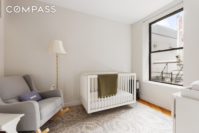 bedroom featuring a nursery area, wood finished floors, and baseboards