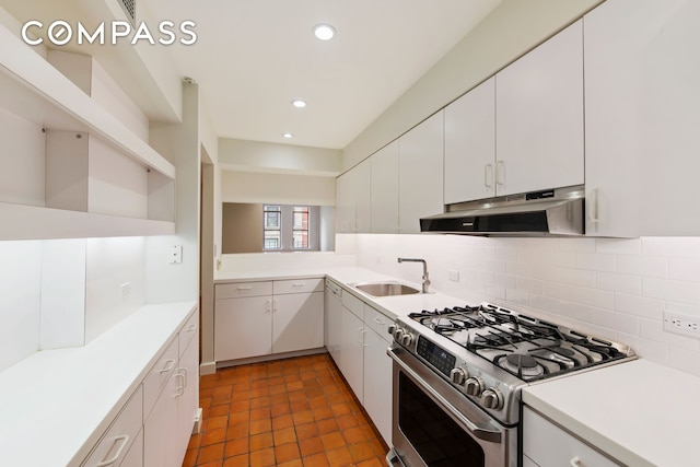 kitchen with stainless steel gas range oven, tasteful backsplash, light countertops, under cabinet range hood, and a sink