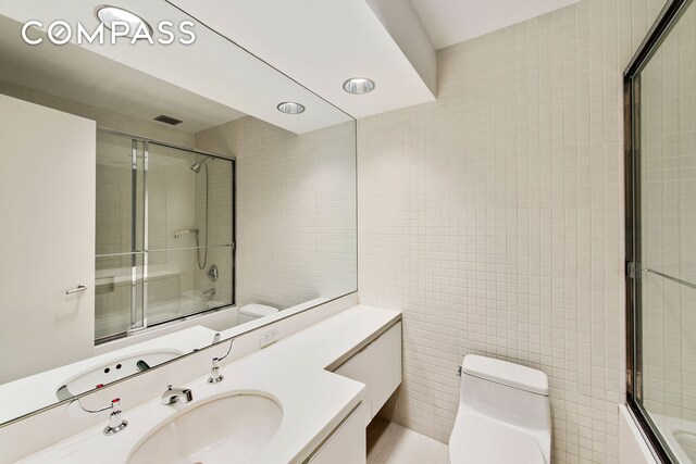 full bathroom featuring combined bath / shower with glass door, vanity, tile walls, and toilet