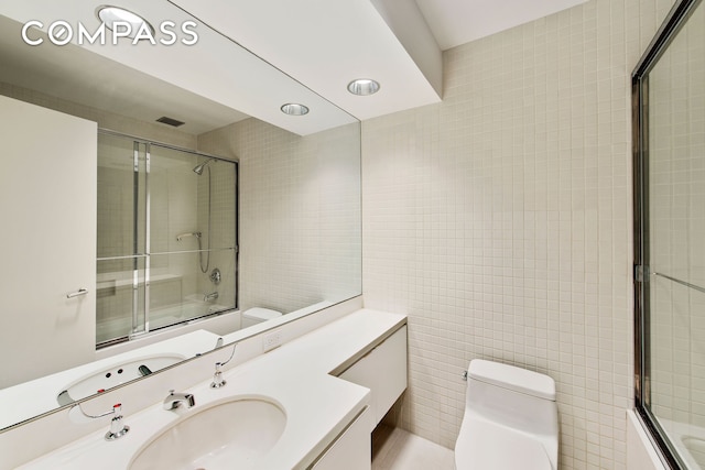 full bathroom featuring tile walls, bath / shower combo with glass door, and toilet