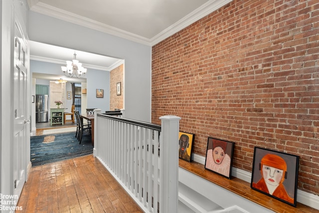 hallway featuring an upstairs landing, a notable chandelier, ornamental molding, wood-type flooring, and brick wall