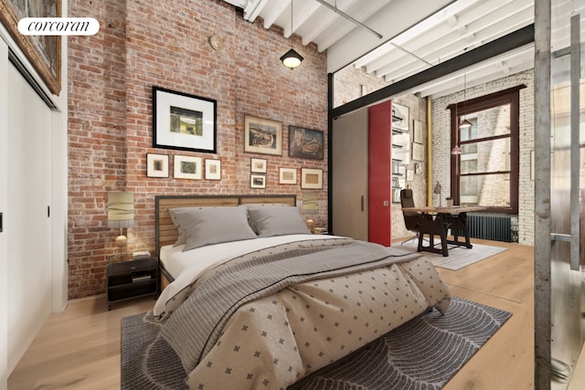 bedroom with radiator, a towering ceiling, brick wall, a closet, and light wood-type flooring