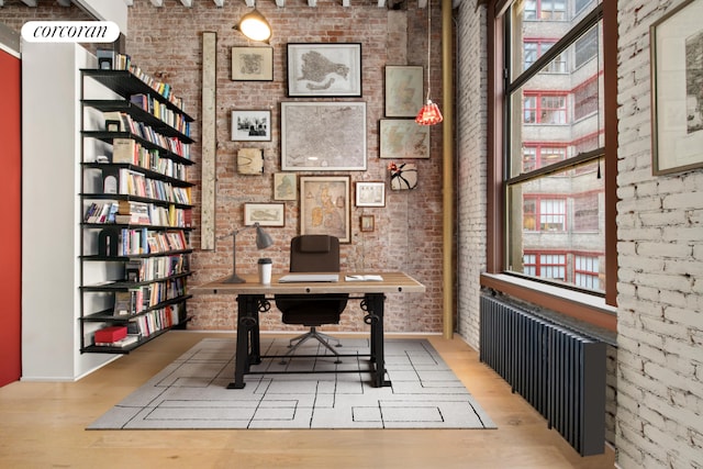 unfurnished office featuring light hardwood / wood-style flooring, radiator heating unit, plenty of natural light, and brick wall