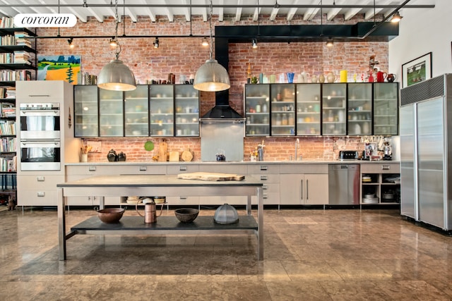 kitchen with hanging light fixtures, stainless steel appliances, and brick wall