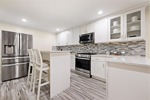 kitchen with backsplash, white cabinets, a kitchen bar, light stone counters, and stainless steel appliances