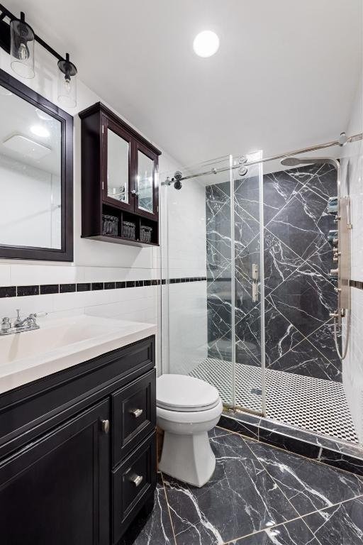 bathroom featuring walk in shower, vanity, toilet, and tile walls