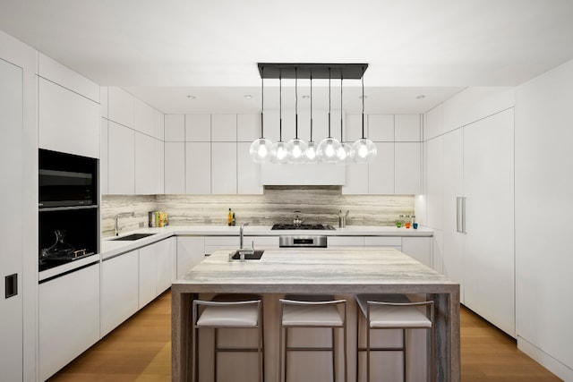 kitchen featuring a breakfast bar area, a sink, white cabinets, light countertops, and a center island with sink