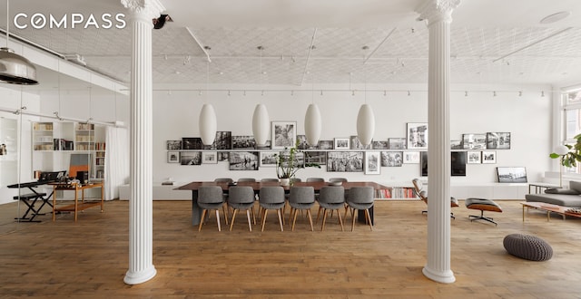 dining space featuring rail lighting, a towering ceiling, ornate columns, and wood finished floors