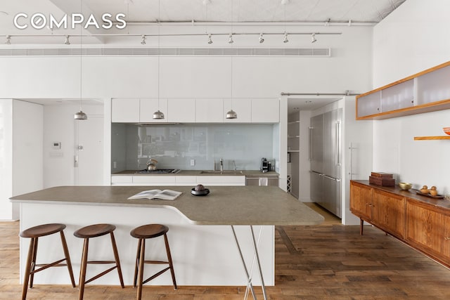 kitchen with a breakfast bar area, tasteful backsplash, stainless steel appliances, white cabinetry, and wood finished floors