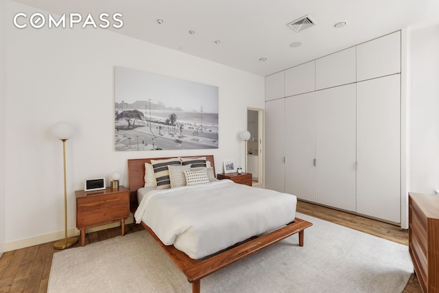 bedroom with a closet, visible vents, baseboards, and wood finished floors