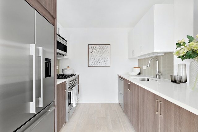 kitchen with light countertops, backsplash, white cabinetry, a sink, and built in appliances