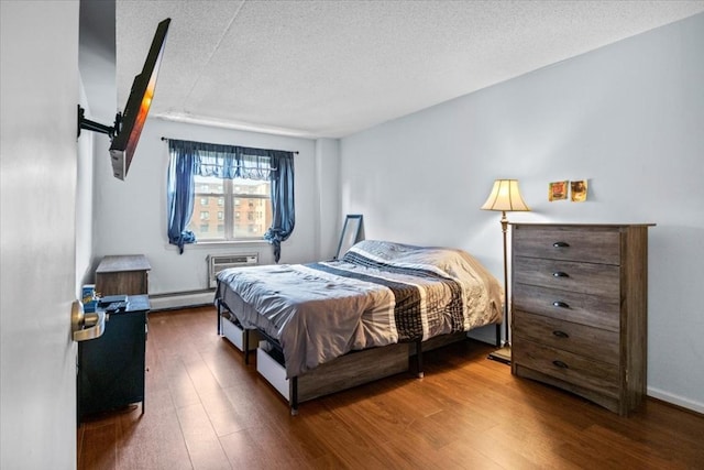 bedroom with dark wood-type flooring, a wall mounted air conditioner, a textured ceiling, and a baseboard heating unit