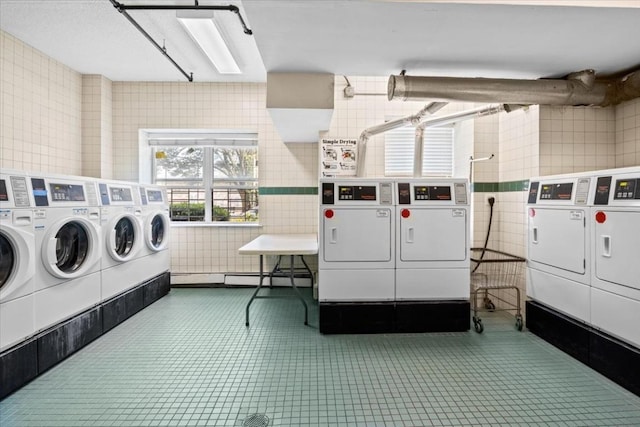 clothes washing area with washing machine and clothes dryer, tile patterned flooring, and tile walls