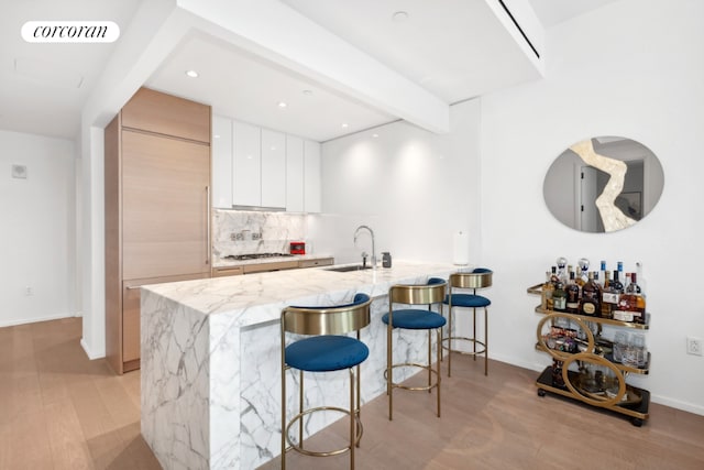 bar featuring beamed ceiling, tasteful backsplash, light stone countertops, white cabinets, and sink