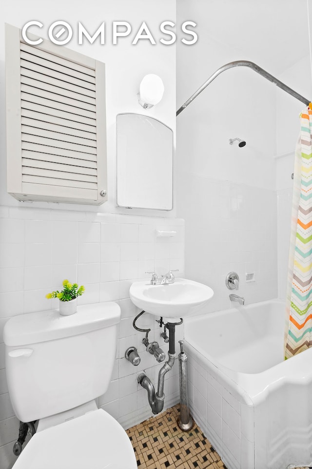 bathroom featuring tile walls, toilet, shower / bath combo with shower curtain, and a sink