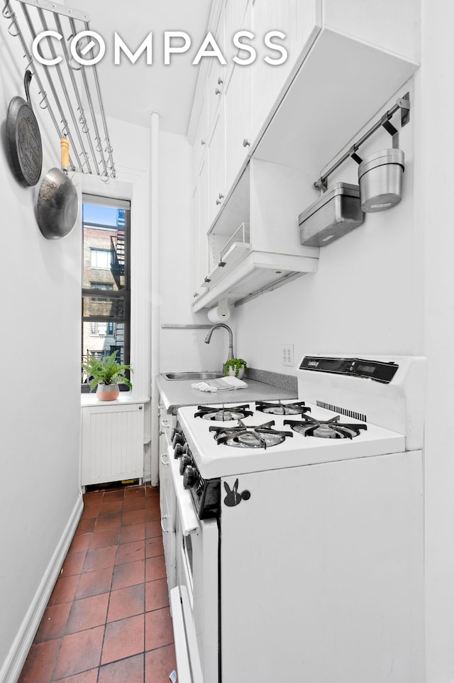 kitchen with dark tile patterned floors, white gas stove, a sink, radiator heating unit, and white cabinets