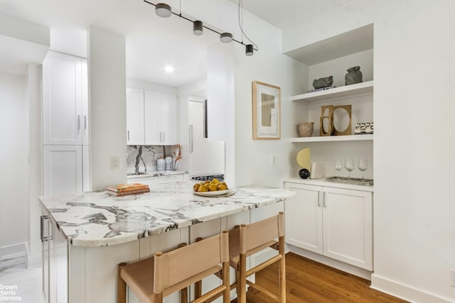 kitchen featuring light stone counters, a breakfast bar, open shelves, backsplash, and white cabinets