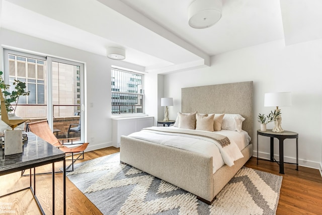 bedroom featuring access to exterior, baseboards, wood finished floors, and beamed ceiling