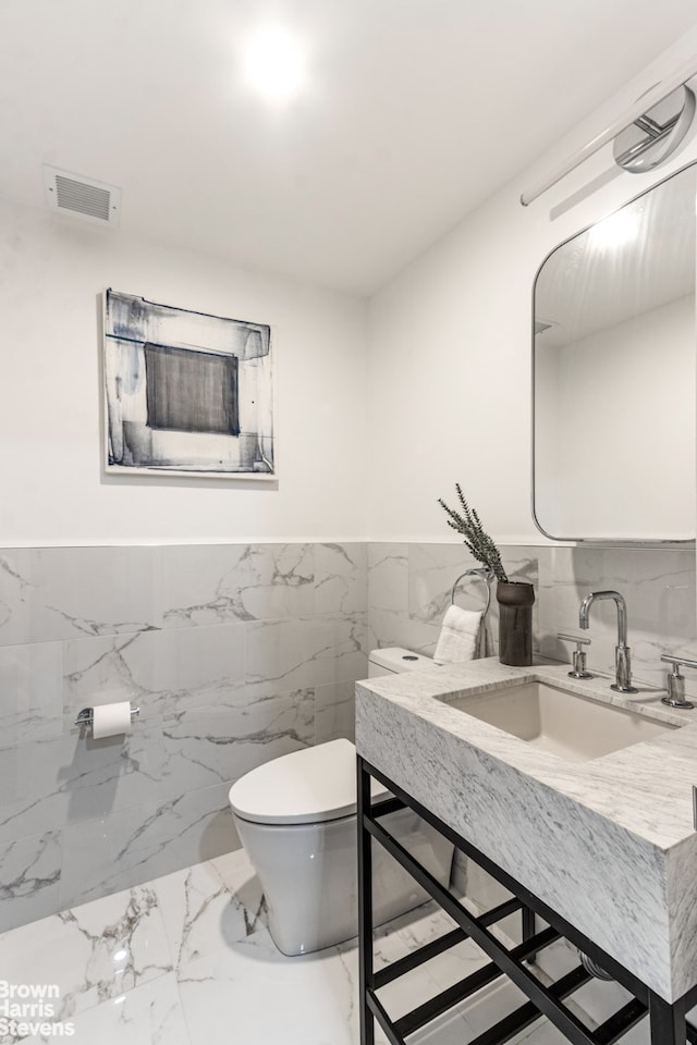 half bath with visible vents, wainscoting, toilet, marble finish floor, and vanity