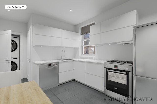 kitchen featuring sink, appliances with stainless steel finishes, white cabinetry, stacked washer / drying machine, and dark tile patterned flooring