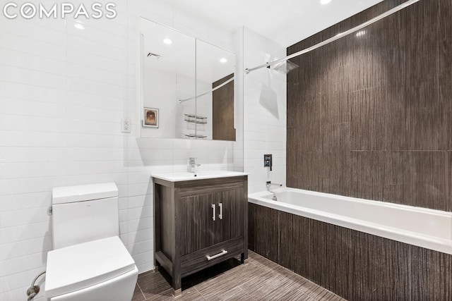 full bathroom featuring vanity, tiled shower / bath combo, tile walls, and toilet