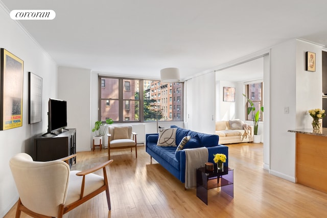 living area featuring light wood finished floors, baseboards, visible vents, and ornamental molding