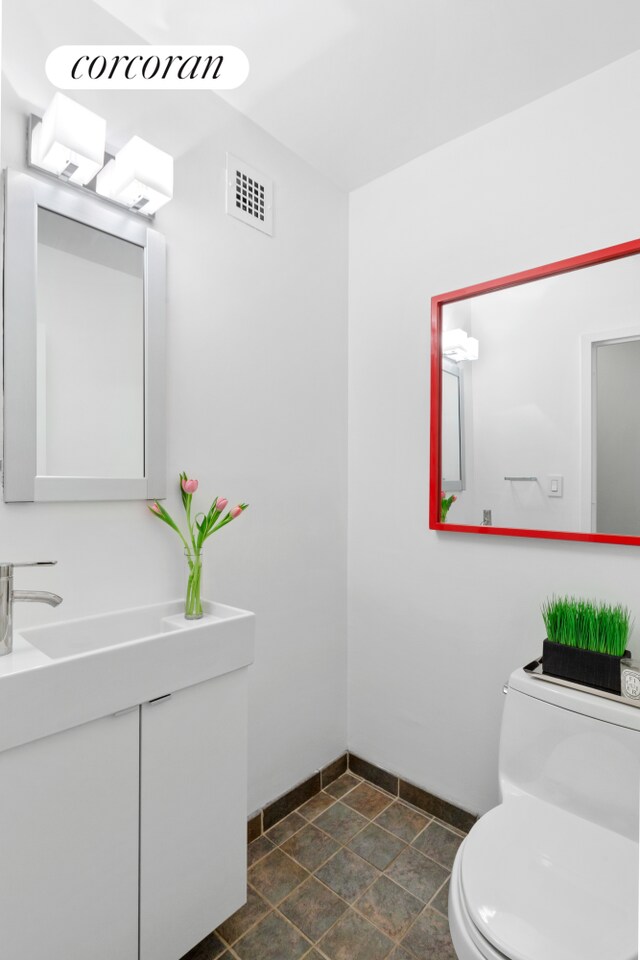 bathroom with toilet, stone finish floor, visible vents, and baseboards