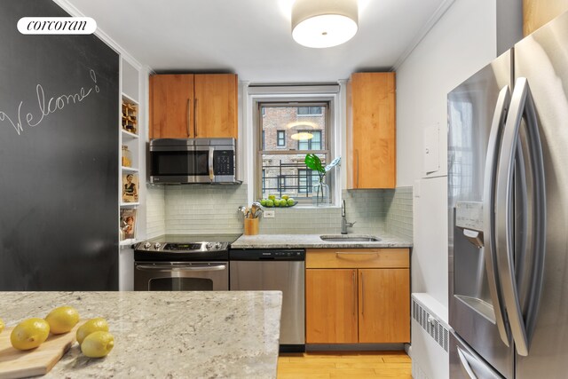 kitchen featuring a sink, light wood-style floors, appliances with stainless steel finishes, backsplash, and radiator