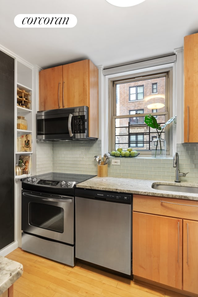 kitchen with appliances with stainless steel finishes, a sink, light stone countertops, light wood-type flooring, and backsplash