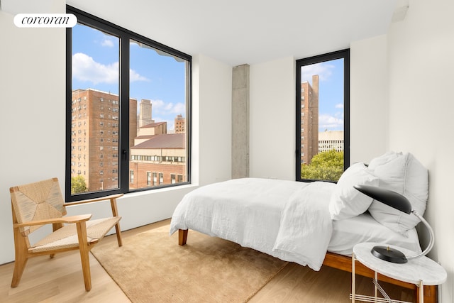 bedroom featuring a view of city, multiple windows, and wood finished floors