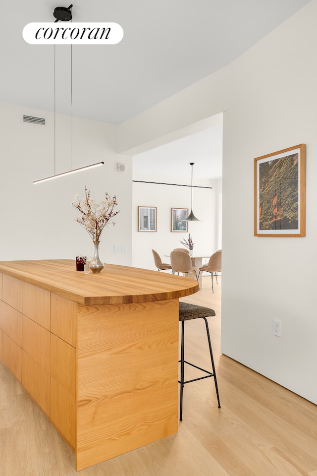 bar featuring light wood-type flooring, visible vents, and pendant lighting