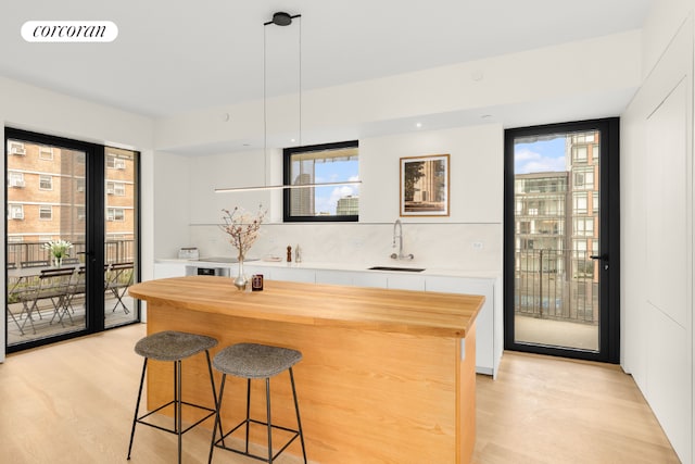 bar with white cabinetry, hanging light fixtures, sink, and light wood-type flooring