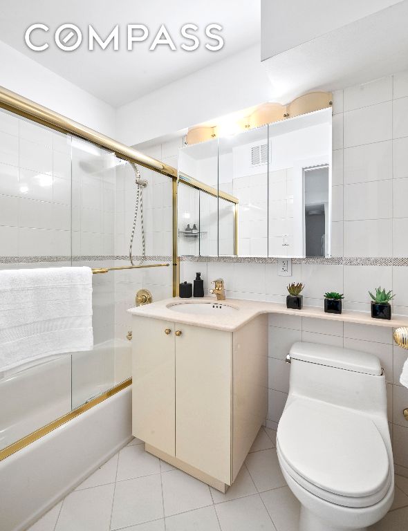 full bathroom featuring enclosed tub / shower combo, tile walls, vanity, tile patterned floors, and toilet