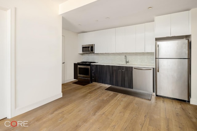 kitchen with decorative backsplash, appliances with stainless steel finishes, light hardwood / wood-style flooring, and white cabinets