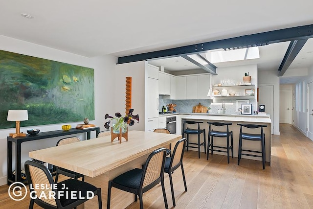 dining room with a skylight, beam ceiling, and light wood-type flooring