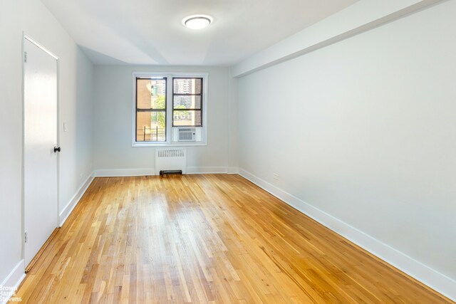 unfurnished room with cooling unit, radiator, baseboards, and light wood finished floors