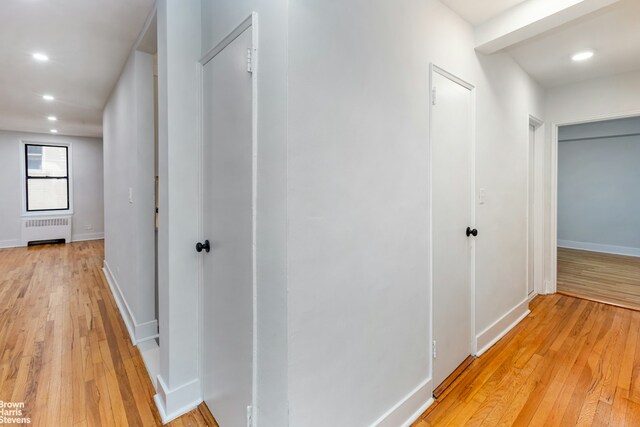 hall featuring light wood-type flooring, radiator, baseboards, and recessed lighting