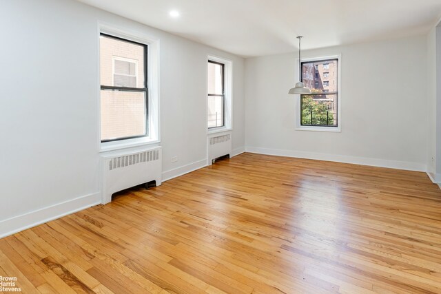 spare room featuring radiator, light wood-style floors, and baseboards