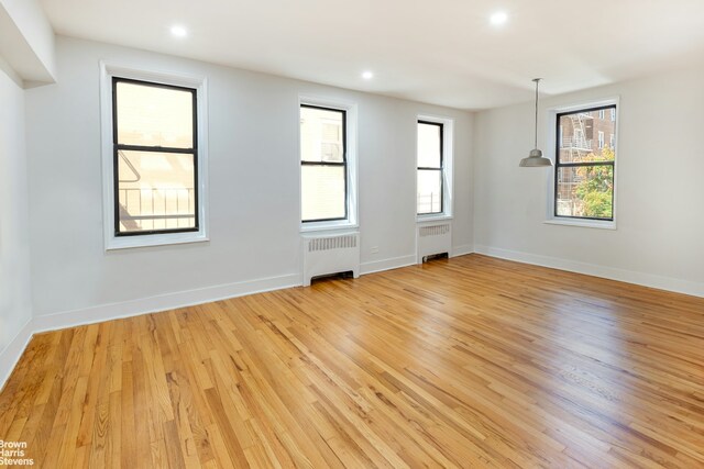 unfurnished room with baseboards, light wood-style flooring, and radiator