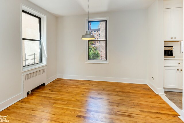 unfurnished dining area featuring light wood-style floors, radiator heating unit, and baseboards