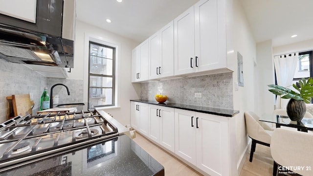 kitchen with white cabinetry, dark stone counters, range with gas stovetop, and tasteful backsplash