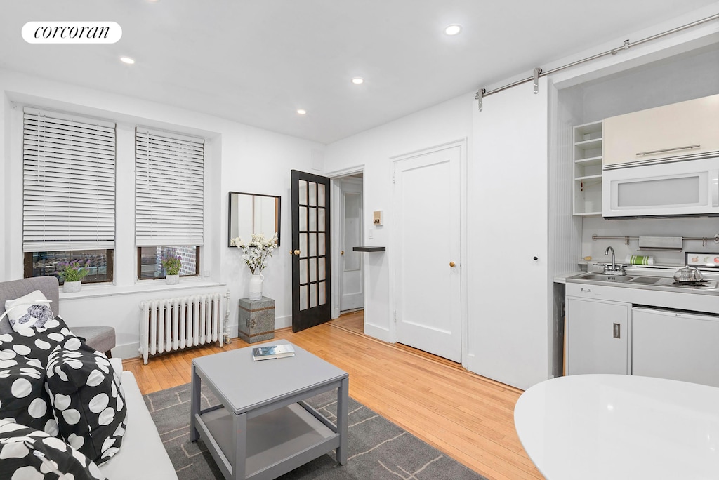 living room featuring a barn door, visible vents, radiator heating unit, light wood-style flooring, and recessed lighting